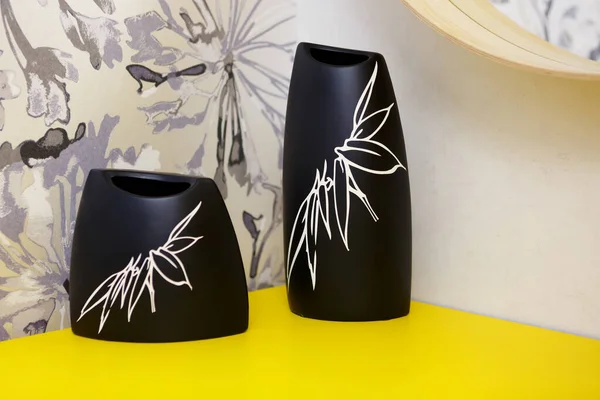 Two black vases on a yellow shelf in a bedroom. On vases a florid pattern. Vases stand in a corner, walls with a pattern of flowers. Interior Design.