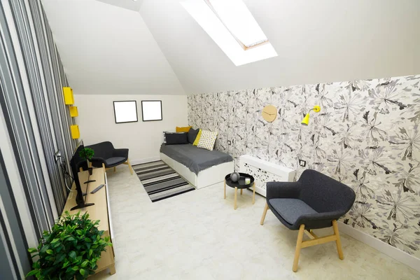 Bedroom room with gray sofa. Gray armchair, bright pillows on the sofa. Floor mat. There are two photo frames on the wall where you can insert your photos. Yellow decorative shelves with flowers on a striped wall.