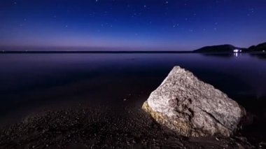 Zaman aşımı. Yıldızlı bir gecede Karadeniz kıyılarında büyük bir taş. Yıldızlar ufukta hareket ediyor. Gökyüzünün mavi ve mor tonları. Dalgalar kıyıya vuruyor.