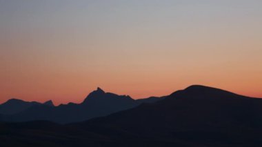 Zaman aşımı 4K. Gün batımında sıradağların siluetleri. Renkli gün batımı, farklı renkler taşmış. Parlak resim, araba trafiği.
