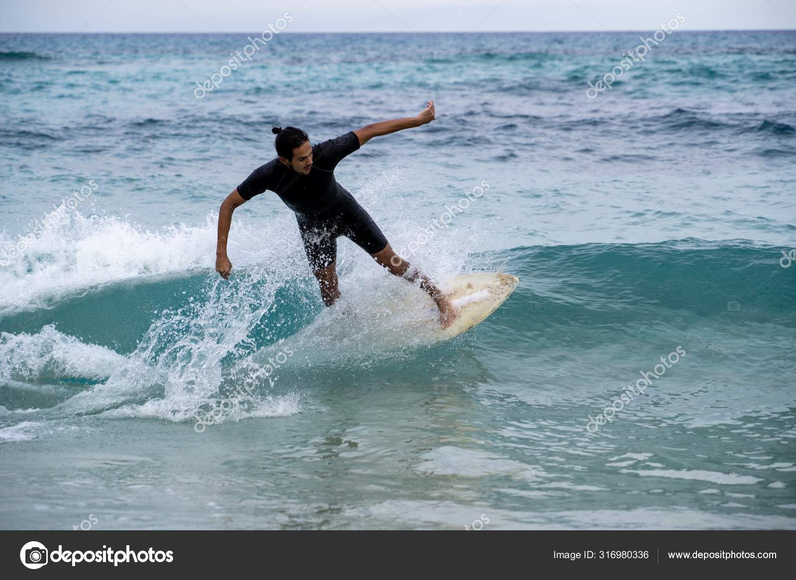 Young man riding a wave on a skimboard (a mix of surf and skate) in