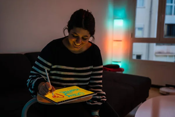 Cute brunette girl drawing on a tablet with a digital pen the words 