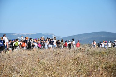İnsanlar, çocuklar ve yetişkinlerden oluşan bir kalabalık kuru çimenlerde yürüyor.,