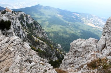 Uçurumdan aşağıdaki manzarada bir fotoğraf çekildi. Aşağıda sık bir orman yetişir ve gökyüzünde bazı yerlerde ağaçların üzerine gölge düşen bulutlar bir resim çeker..