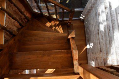 Odada ahşap bir sarmal merdiven var. Vitrinden, tahta merdivenlere ve korkuluklara ışık düşüyor. Tırmanmak için merdivenler, görünen tahta kirişler beyaza boyanmış..