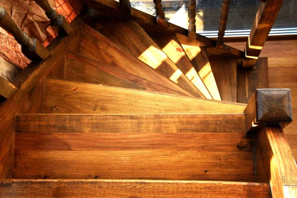 A wooden spiral staircase is located in the room. From stained glass, light falls on wooden steps and railings. Ladder to climb up.