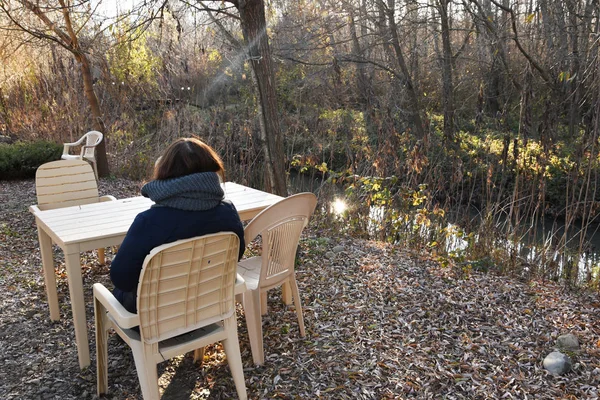 The girl sits on a plastic chair at the table and admires nature. Quiet weather, relaxation in the park and tranquility in nature.
