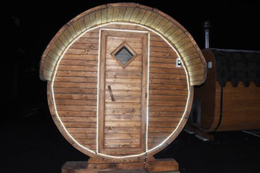 Gezici bir sauna, ahşap fıçı şeklinde bir banyo geceleri sokakta durur. Tahta varilin girişi kurşun şeritle çevrili. Gezici sauna, ahşap banyo..