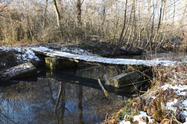 Küçük ahşap bir köprü karla kaplıdır. Sokakta, sonbaharda, dünyanın bazı yerlerinde kar var ve buzlar görülebilir. Nehrin sularında sonbahar ağaçlarının yansımaları görülebilir.
