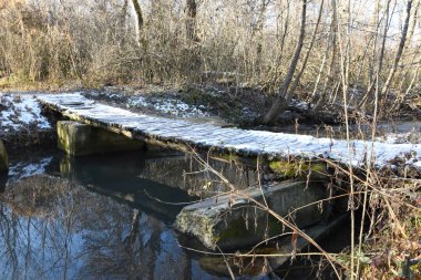 Küçük ahşap bir köprü karla kaplıdır. Sokakta, sonbaharda, dünyanın bazı yerlerinde kar var ve buzlar görülebilir. Nehrin sularında sonbahar ağaçlarının yansımaları görülebilir.