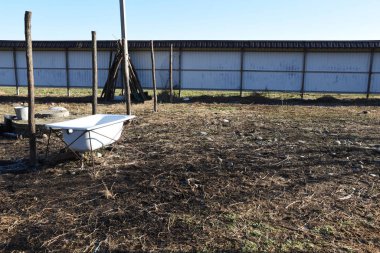 Avluda demir bir çitin arkasında demir bir küvet var. Bahçeye saman ve beyaz bir küvet saçılmış..