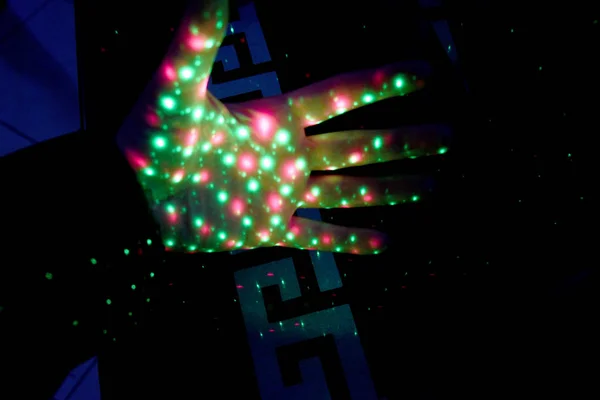 A hand with an open palm, multi-colored lights are visible on the whole hand and fingers, many colorful lights decorate the night.
