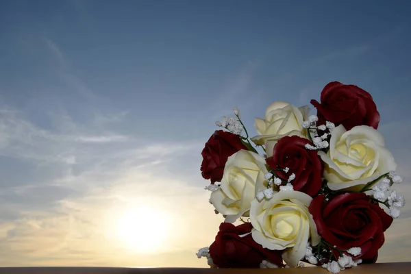 A bouquet of bright roses made from soap, located on nature against the backdrop of the sunset. A bouquet of red and white roses, sunset, rays and clouds, a beautiful postcard for the holiday.