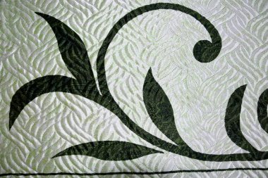 Gümüş bir kumaşta, yeşil desenin bir kısmı karalamalar ve çizgiler şeklinde görünür..