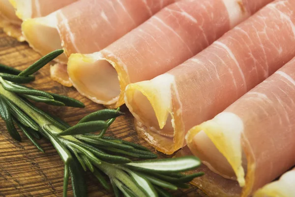 Tunna skivor prosciutto med rosmarin på trä skärbräda, vintage bakgrund. Isolerad på vit bakgrund — Stockfoto