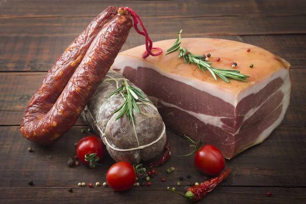 Italský salám, prosciutto šunka a pikantní klobása s cherry rajčátky a červenou paprikou a kořením zblízka na dřevěné pozadí — Stock fotografie