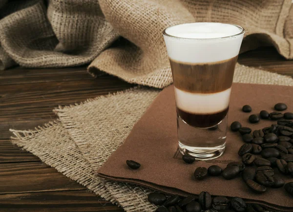 Coffee Latte. Coffee with whipped cream topping  in a tall glass on a wooden background with burlap