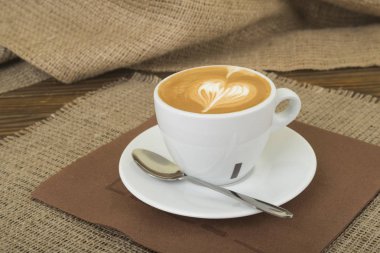 Çuval bezi arka plan ile ahşap bir masa üzerinde sıcak latte sanat kahve Kupası c daire