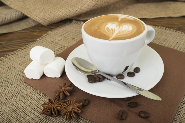 Varm latte art kaffe kopp c tefat på ett träbord med säckväv bakgrund — Stockfoto