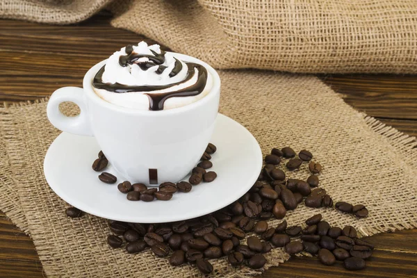 Kahve Latte. Çuval bezi ahşap bir zemin üzerine uzun bir bardak krem şanti tepesi ile kahve — Stok fotoğraf