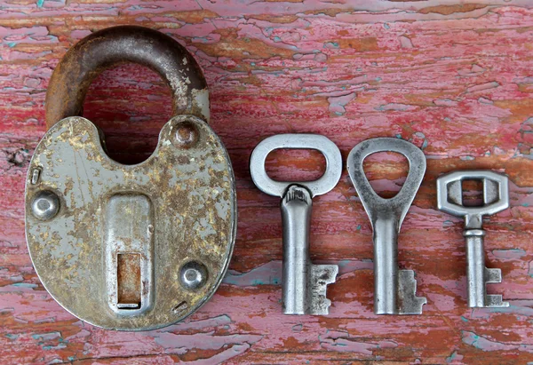 Vecchia serratura arrugginita con tre chiavi diverse sulla superficie di legno — Foto Stock