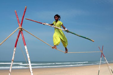 GOA, INDIA - FEB 12: Wandering indian tightrope walker playing on the beach of Goa, on Feb 12, 2008. Small groups of buskers traveling along the coast and arrange free shows for tourists on the beach clipart
