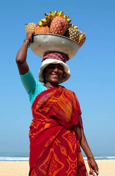 Goa, Indien - 18 Feb, 2008: Vackra frukt leverantör på stranden av Arabiska havet. Indiska kvinnor föredrar att bära tunga saker på huvudet — Stockfoto