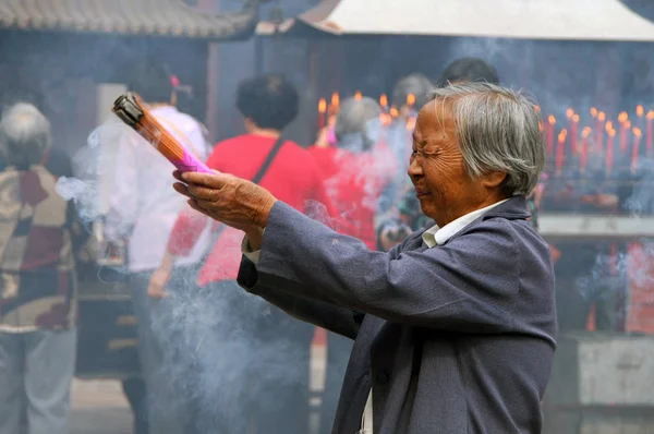 ZHUJIAJIAO, CHINA - OCT 29, 2009: Chinese elderly woman praying in the buddhist monastery. In Buddhism, incense sticks are an important part of religious rituals — Stock Photo, Image