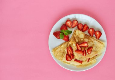 Kahvaltıda ev yapımı gözleme ile dilimlenmiş çilek. Pembe arka planda beyaz bir plaka. Metin için boş alan.
