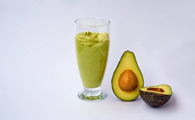 Bir bardak avokado ve ıspanaklı smoothie ve beyaz arka planda yarım avokado. Fitness ürünü. Beslenme sporları beslenmesi.