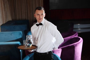 Genç, yakışıklı bir garson bir sürahi suyun içinde tepsi tutuyor. Restoran işi kavramı. Restoran işindeki çalışanlar..