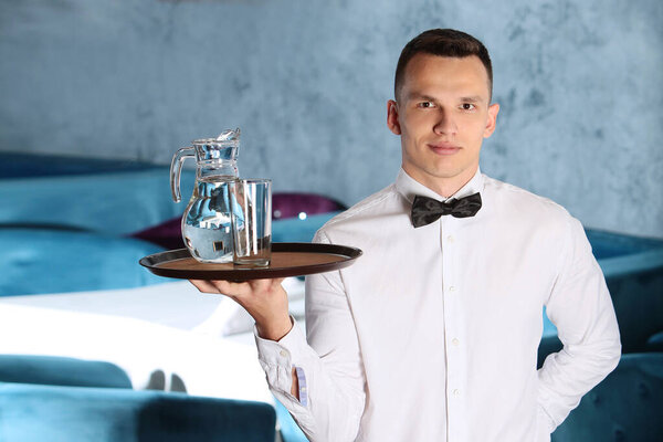 Молодой красивый официант держит поднос в графине с водой. Концепция ресторанного бизнеса
.