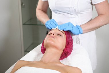 Bir kozmetikçi, hastanın cildini beslemesi, nemlendirmesi ve tazelemesi için yüzüne bir ilaç koyar. Klinikte estetik ameliyat. Hastanın yüzüne yakın çekim..