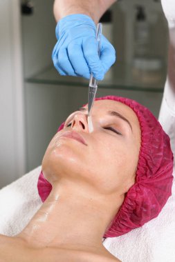 Bir kozmetikçi, hastanın cildini beslemesi, nemlendirmesi ve tazelemesi için yüzüne bir ilaç koyar. Klinikte estetik ameliyat. Hastanın yüzüne yakın çekim. Güzellik bürosu