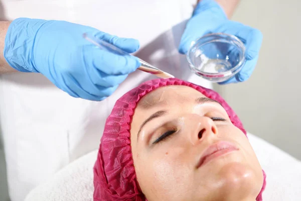 Un cosmetólogo pone un remedio en la cara para que el paciente nutra, hidrata y rejuvenece la piel. Procedimiento de cosmetología en la clínica de cosmetología . — Foto de Stock