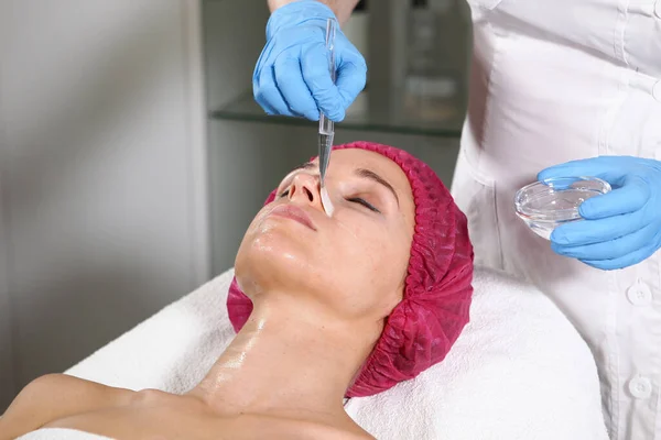 Bir kozmetikçi, hastanın cildini beslemesi, nemlendirmesi ve tazelemesi için yüzüne bir ilaç koyar. Klinikte estetik ameliyat. Hastanın yüzüne yakın çekim. Güzellik bürosu