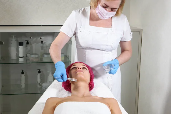 Un cosmetólogo pone un remedio en la cara para que el paciente nutra, hidrata y rejuvenece la piel. Procedimiento de cosmetología en la clínica de cosmetología.Oficina esteticista — Foto de Stock