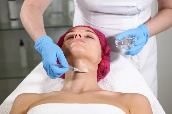 Un cosmetologo mette un prodotto sul collo del paziente per nutrire, idratare e ringiovanire la pelle. Procedura estetica in clinica. Primo piano del volto del paziente. Ufficio estetista — Foto Stock