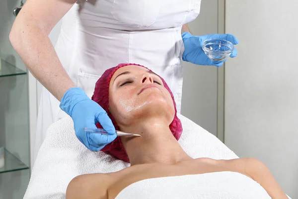 En kosmetolog sätter en produkt på patientens hals för att ge näring, återfukta och vitalisera huden. Kosmetisk procedur på kliniken. Närbild av patientens ansikte. Vackert kontor — Stockfoto