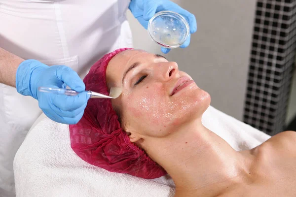 Primo piano del volto del paziente nello studio di cosmetologia. Applicare sul viso significa idratare e ringiovanire la pelle. lifting facciale non chirurgico. Spazzola con il farmaco nelle mani di un estetista . — Foto Stock