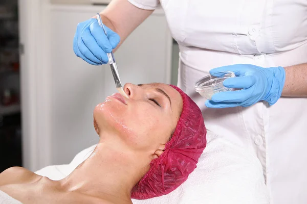 Primer plano de la cara del paciente en el consultorio de cosmetología. Aplicar en la cara significa hidratar y rejuvenecer la piel. lifting facial no quirúrgico. Cepillo con la droga en las manos de un esteticista . — Foto de Stock