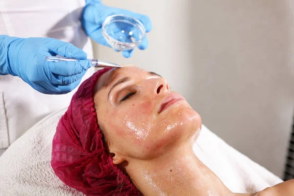 Primer plano de la cara del paciente en el consultorio de cosmetología. Aplicar en la cara significa hidratar y rejuvenecer la piel. lifting facial no quirúrgico. Cepillo con la droga en las manos de un esteticista . — Foto de Stock