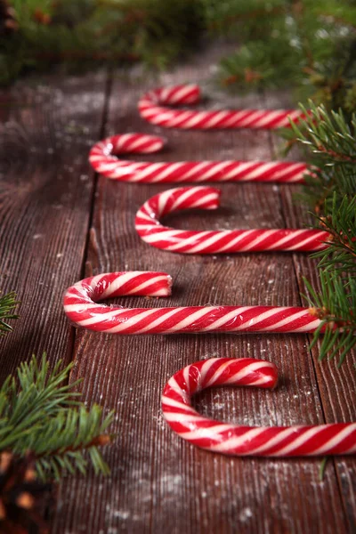 Sweet candy made of caramel in the form of a cane on a wooden background and with fir branches. Place an inscription or label. The concept of New year or Christmas holidays Out of focus.