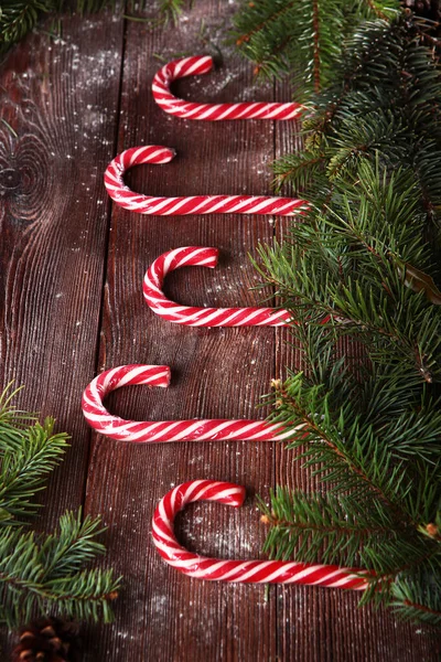Sweet candy made of caramel in the form of a cane on a wooden background and with fir branches. Place an inscription or label. The concept of New year or Christmas holidays Out of focus.