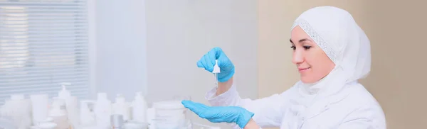 Moslim arts cosmetoloog houdt in haar handen een pipet met een kosmetologisch product. Lange banner voor website design. Kopieerruimte. — Stockfoto