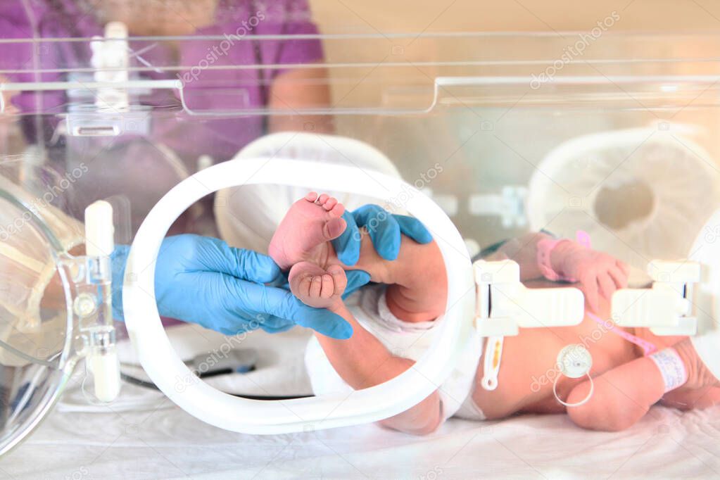 Three-day-old newborn baby in intensive care unit in a medical incubator. Macro photo of doctor's hands and legs of a child. Newborn rescue concept. The work of resuscitation doctors.