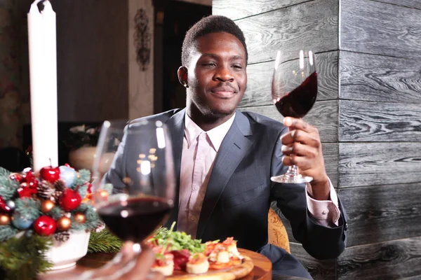Retrato de un empresario afroamericano con una copa de vino en la mano. Empresario en traje y en el interior del restaurante con accesorios navideños en el fondo de la chimenea . — Foto de Stock