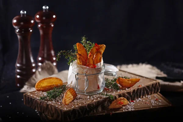 Chips av stekt potatis i en glasburk med svart bakgrund. Pommes frites på en träskiva. Stilleben. — Stockfoto