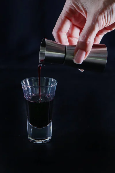 Hand pouring a measuring cup of alcoholic beverage into a glass. Photo on a black background. Copy space. Still life concept — Stock Photo, Image