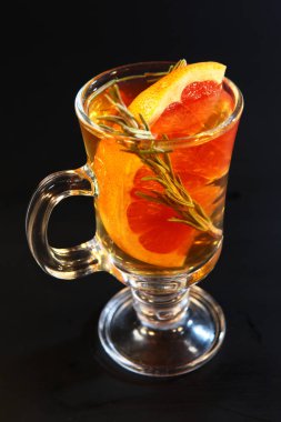 Sıcak çay, greyfurt ve cam bir şişede siyah arka planda otlar. Aroma. Kullan..